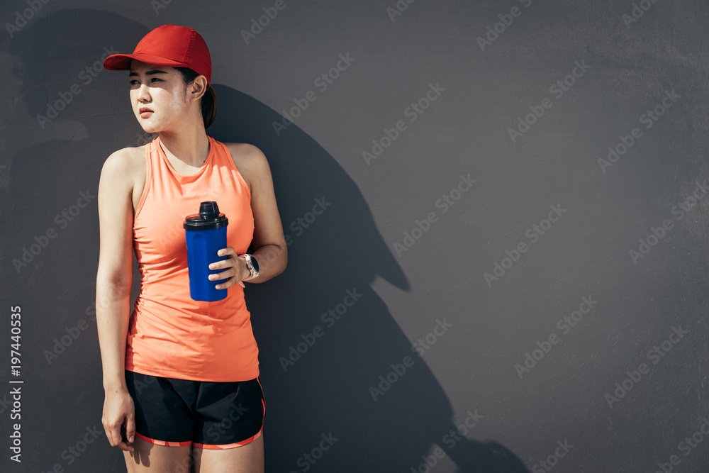 An asian woman athletic is jogging on the concrete road, she is warming her body and tideten her tyi