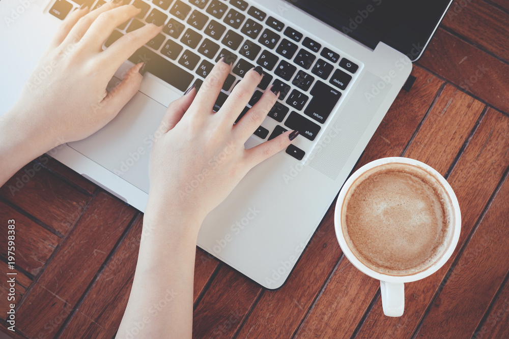 Female hand on laptop using portable laptop working on wooden table in coffee shop