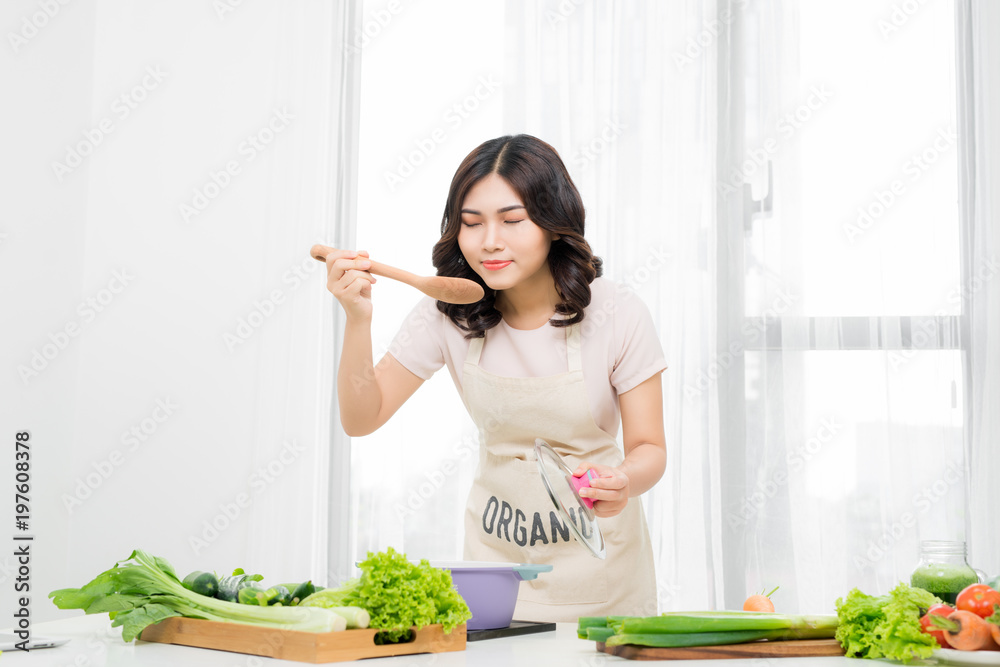 美丽的年轻女子在家用蔬菜煮汤的肖像。