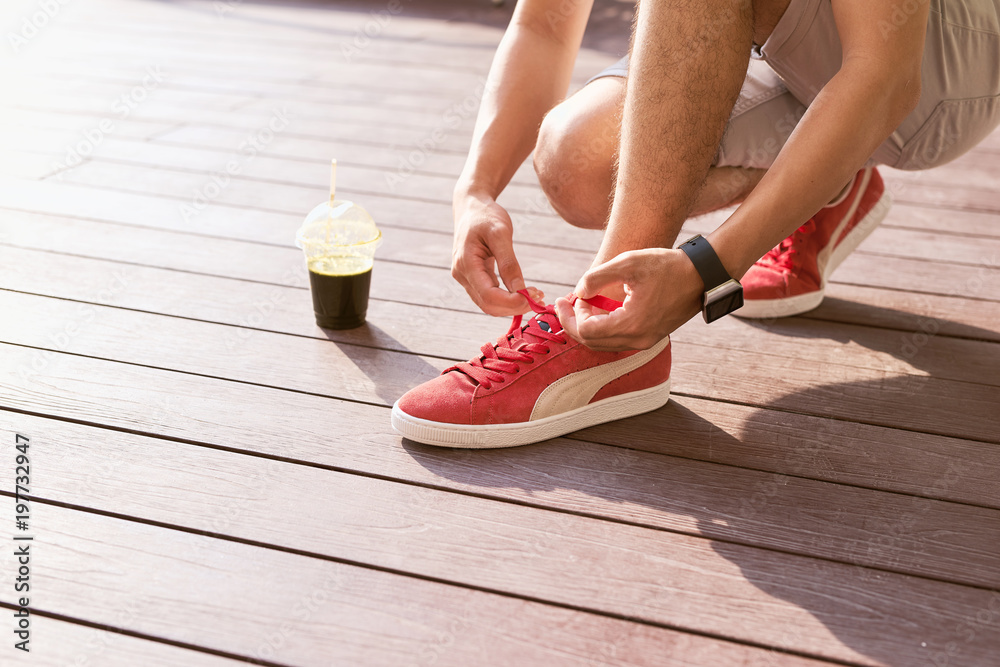 Unrecognizable young runner tying his shoelaces outdoors.