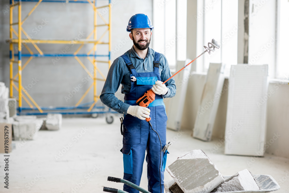 一名身穿工作服的建筑工人手持钻机站在室内施工现场的画像