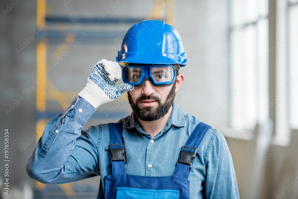 Close-up portrait of a handsome bearded builder with protective glasses and helmet indoors