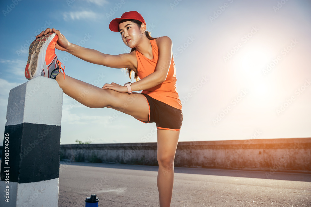 An asian woman athletic is jogging on the concrete road, she is warming her body and tideten her tyi