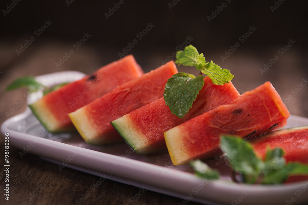 Fresh sliced watermelon in white dish on wooden table.