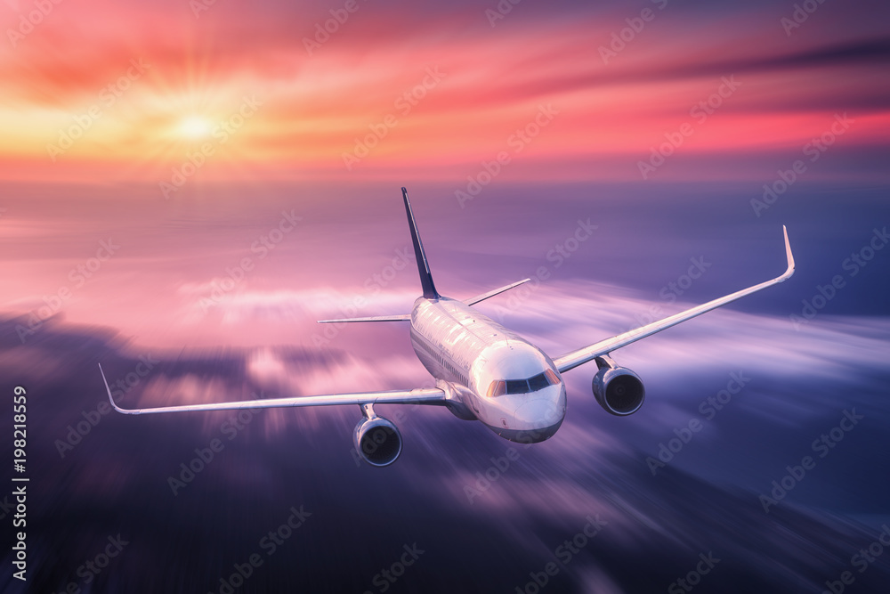 Modern airplane with motion blur effect is flying over low clouds at sunset. Passenger airplane, blu