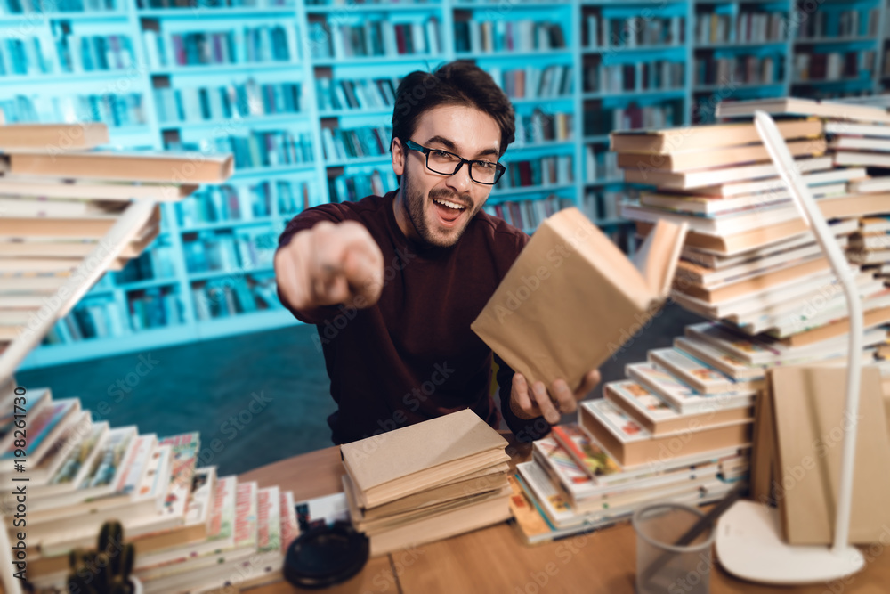 White guy surrounded by books in library. Student is emotionally reading book.