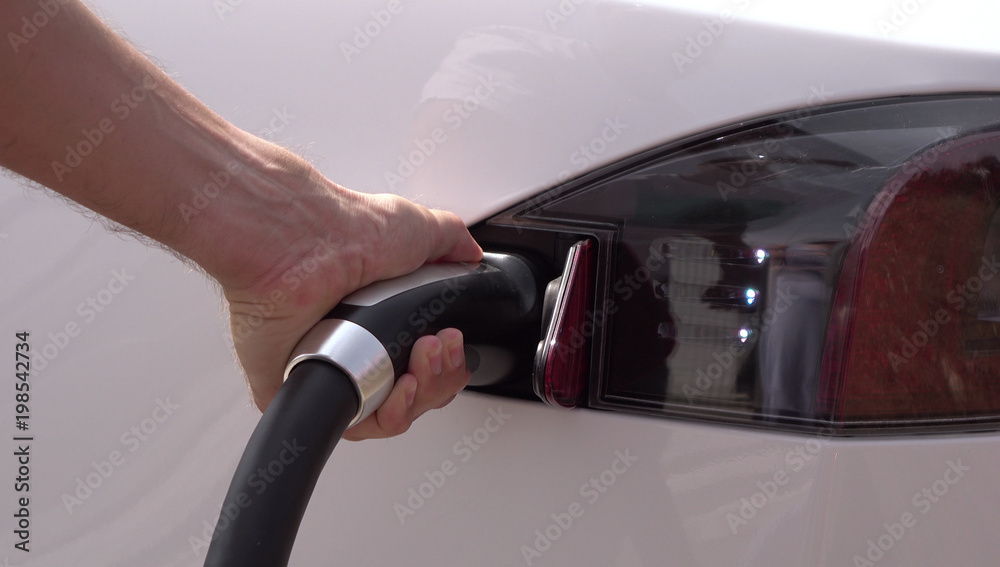 CLOSE UP: Young man plugging in Tesla white electric car at charging station