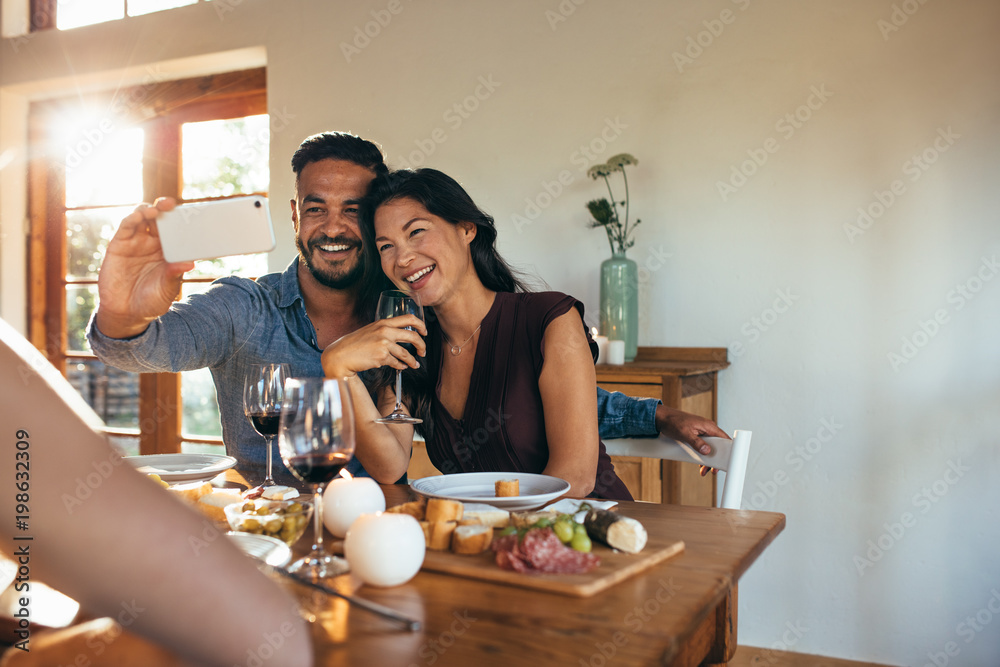 Couple taking selfie at dinner party with friends