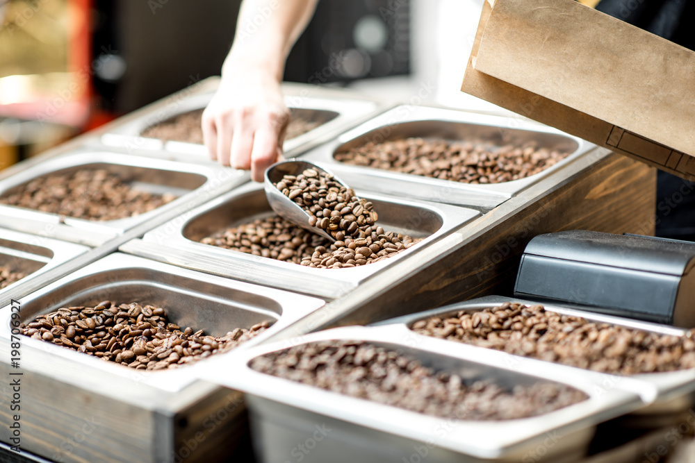 Filling paper bag with coffee beans from the metal trays for selling in the store