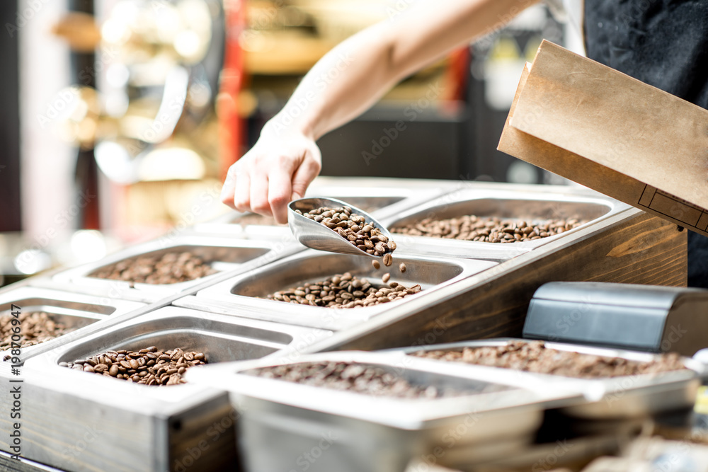 Filling paper bag with coffee beans from the metal trays for selling in the store