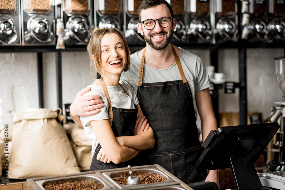 Portrait of a young couple of baristas standing together at the counter of the coffee store