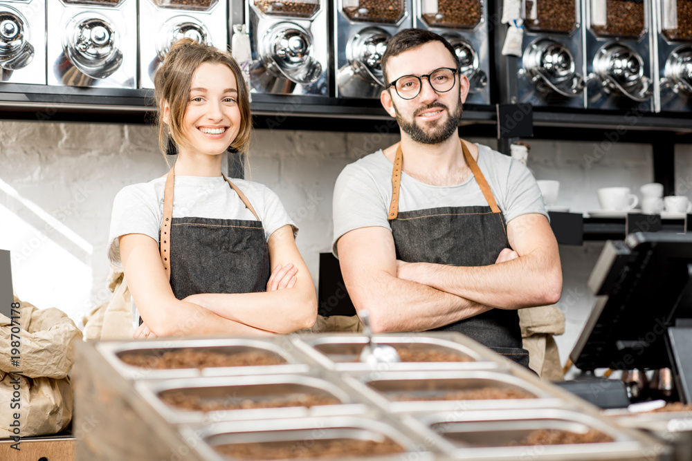 Portrait of a young couple of baristas standing together at the counter of the coffee store