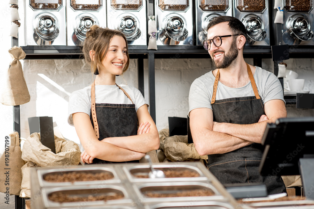 Portrait of a young couple of baristas standing together at the counter of the coffee store