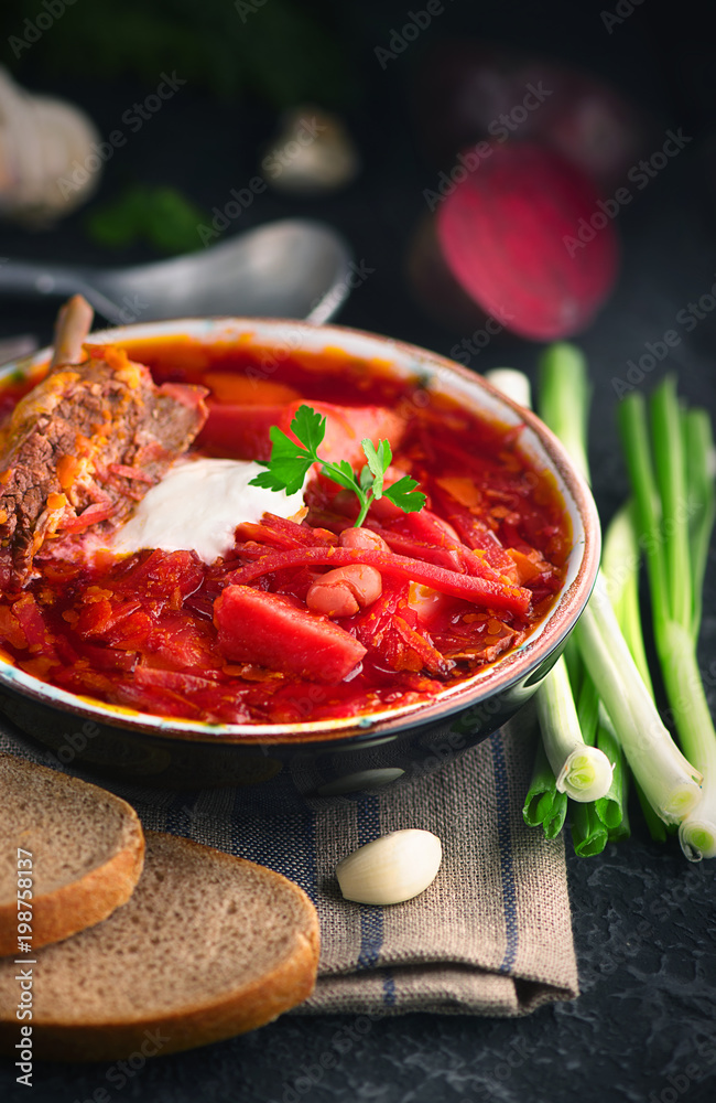 Traditional Ukrainian russian borscht. Plate of red beet root soup borsch on black rustic table. Bee