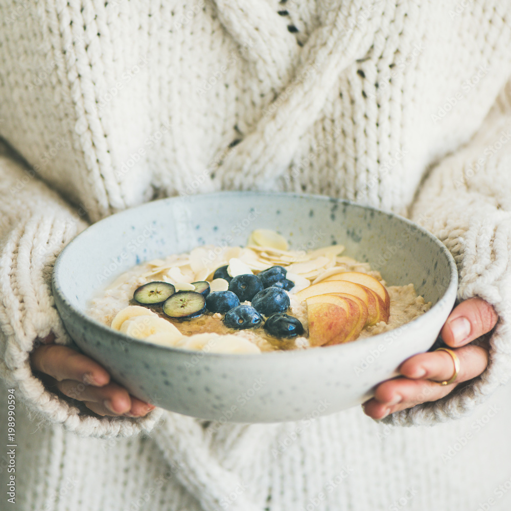 床上的健康冬季早餐。穿着羊毛衫的女人拿着一碗纯素食杏仁奶燕麦片p