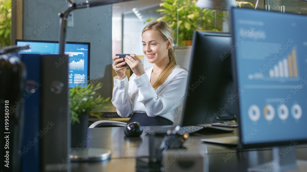 办公室里有魅力的女商人在智能手机上玩电子游戏。微笑的美女