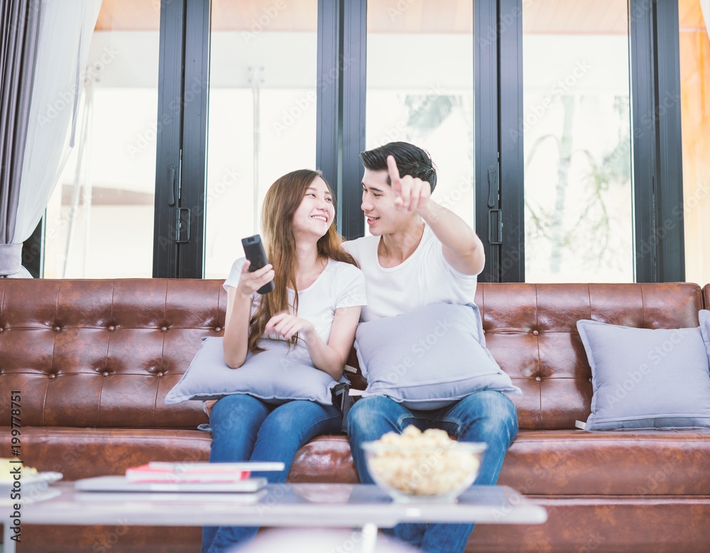 Couple on sofa with TV remote watching television in living room