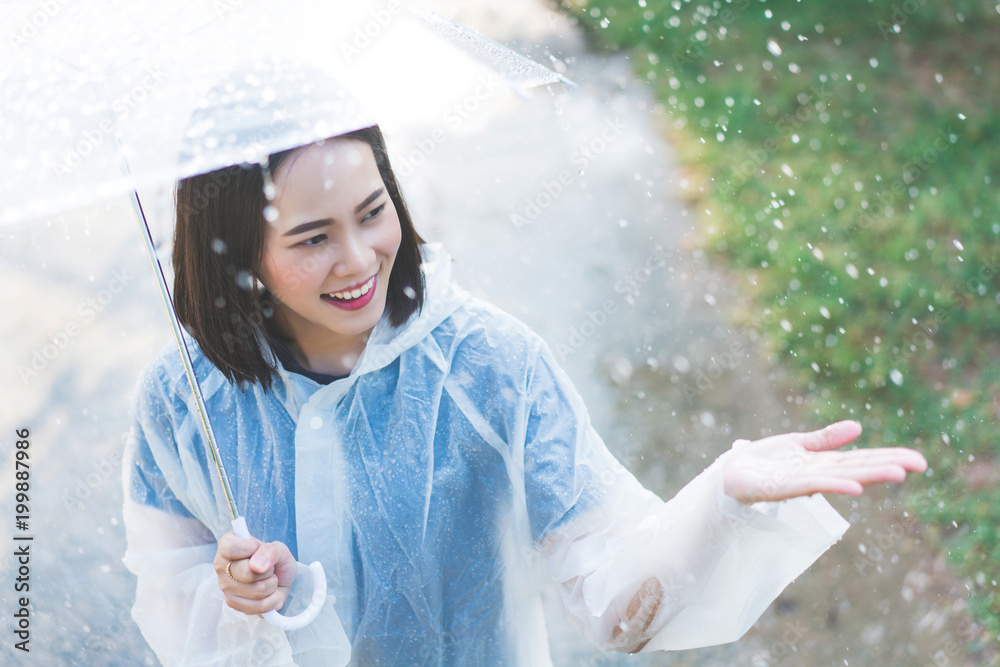 雨天，一个亚洲女人在户外穿着雨衣。她很开心。她用手触摸了雨水。