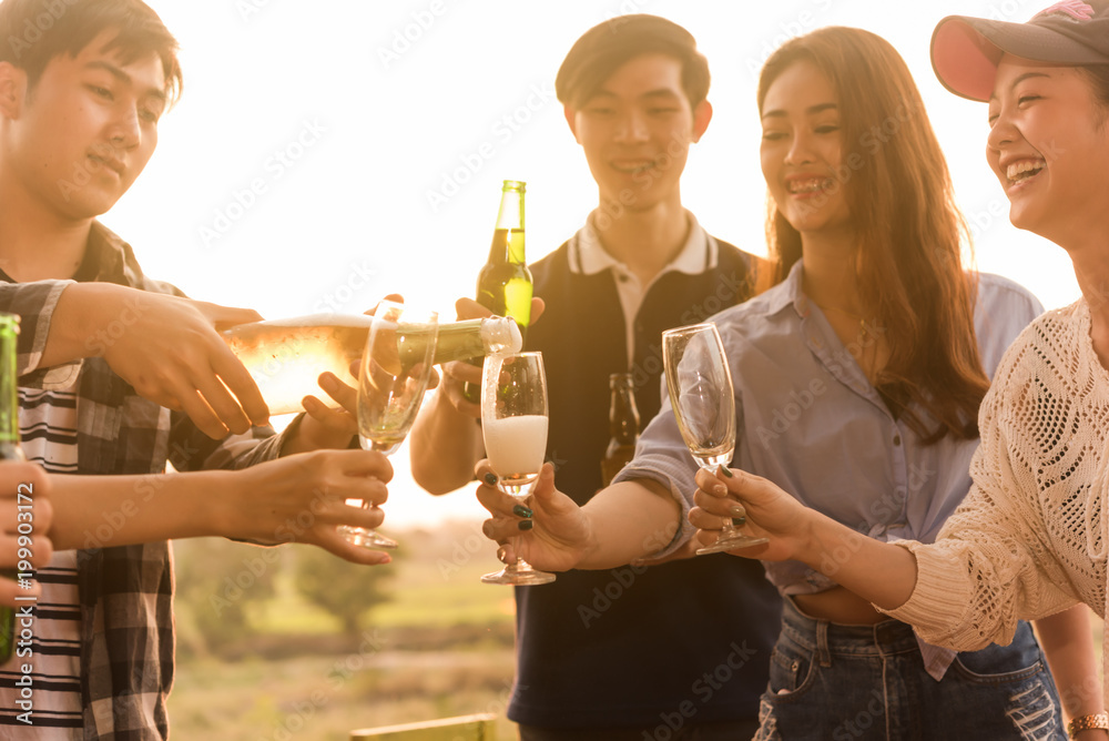 日落时分，6人一组的青少年举行晚宴庆祝，将香槟倒进玻璃杯