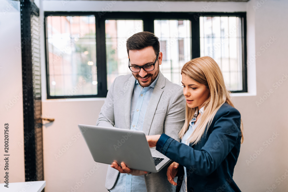 Young business man holding a laptop while discussing new project with his female collegue