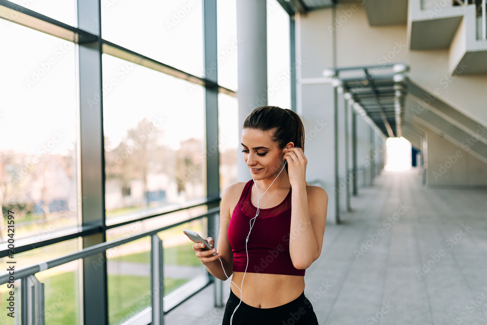 Sporty girl with earphones listening music on her smartphone. Preparing for workout.