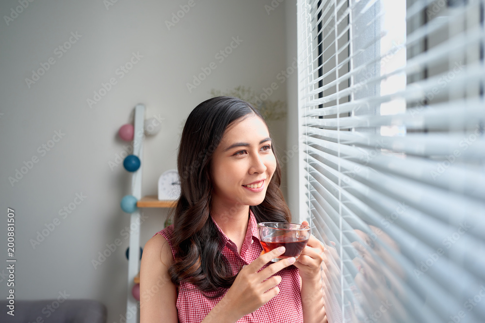 站在办公室窗户边喝茶的年轻女人。