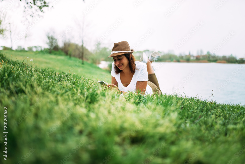 美丽的快乐女人在春天躺在绿草上打电话。