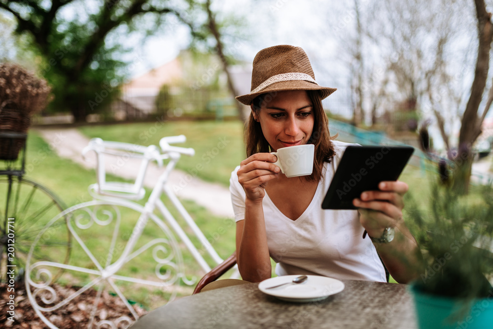 Attractive woman in cafe garden drinking coffee and using tablet.