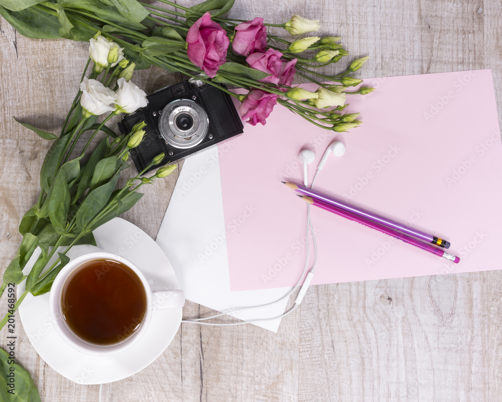 一杯茶、鲜花、老式相机、耳机、铅笔和一张纸的俯视图