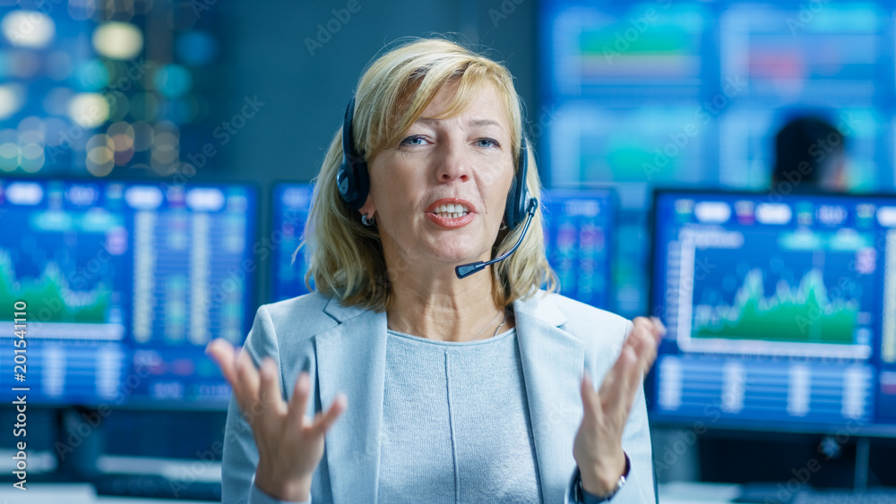 Chief Sales Force Representative Speaks to the Camera. Behind Her People Working, Screens Show Stock