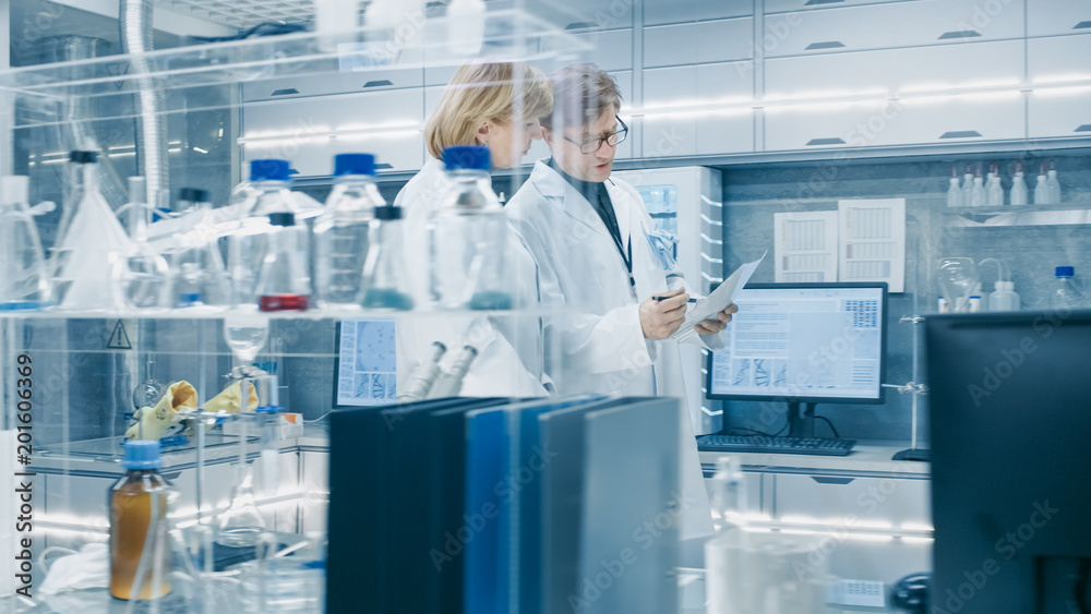 Female and Male Senior Scientists Walking Through Busy Modern Laboratory. They Have  Discussion abou