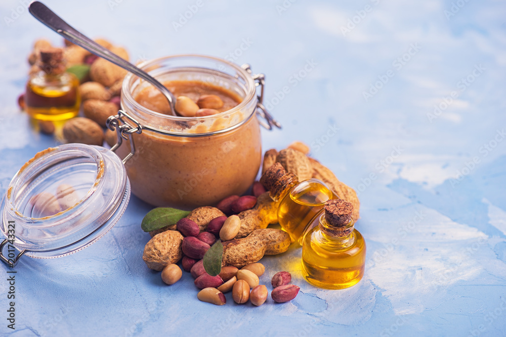 Natural peanut butter with oil in a glass jar and peanuts