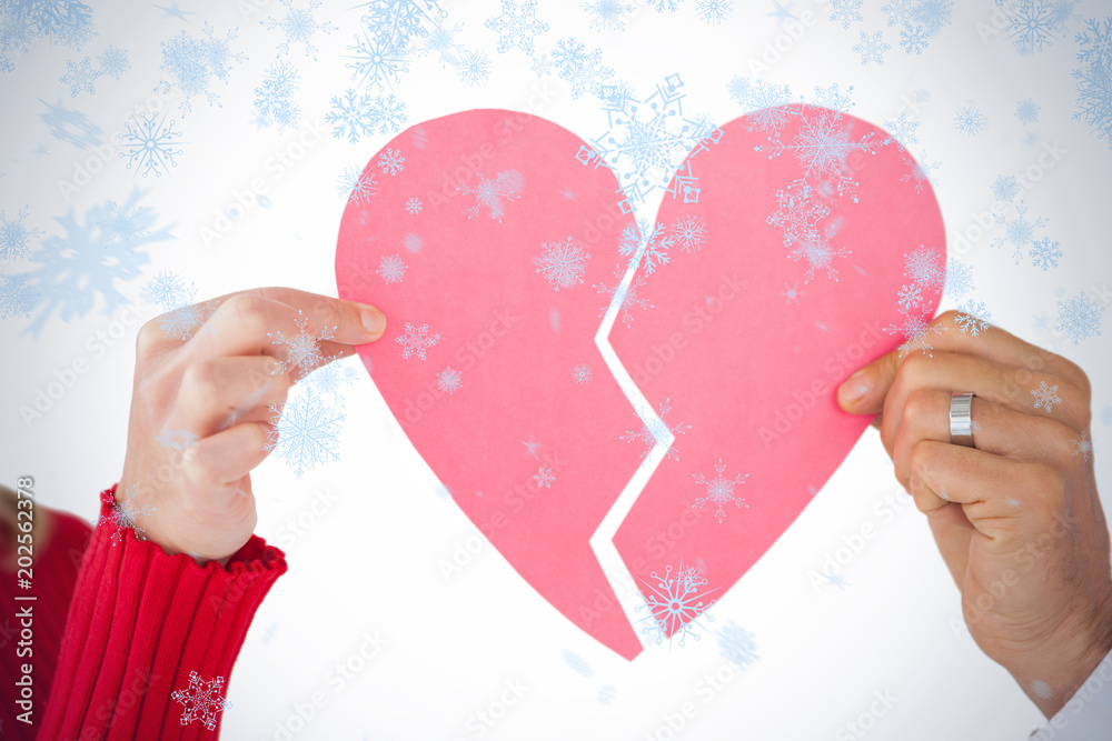 Couple holding two halves of broken heart against snow falling