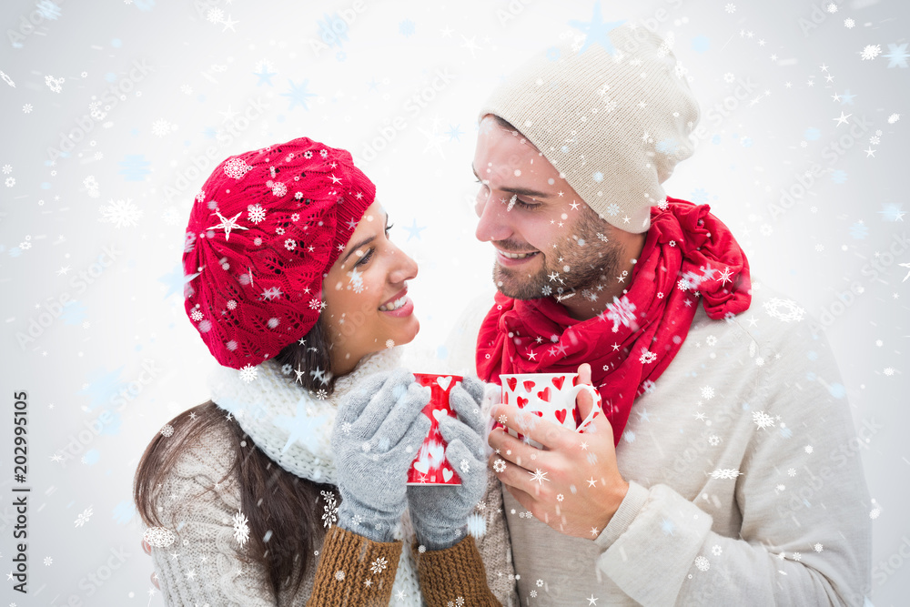 一对穿着保暖衣服、拿着马克杯抵御降雪的迷人年轻夫妇