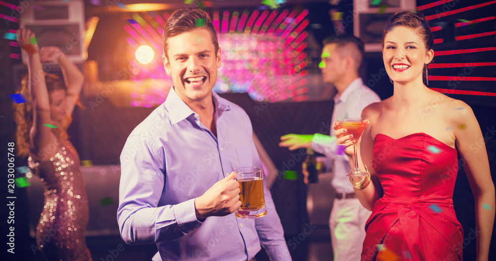 Smiling couple holding glass of beer and cocktail while dancing against flying colours