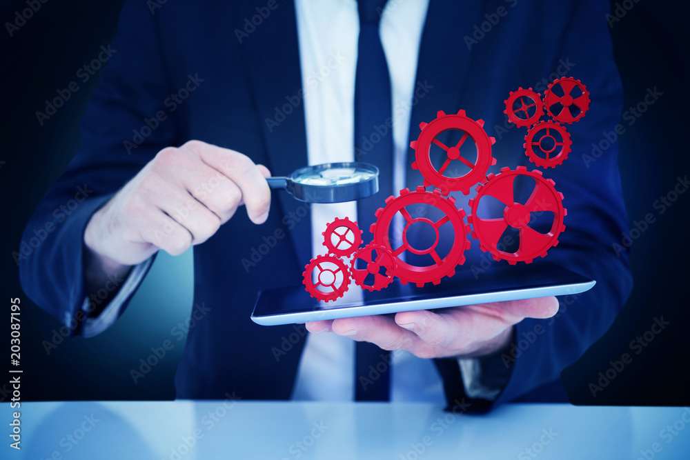 Businessman looking at his tablet through magnifying glass against blue background with vignette