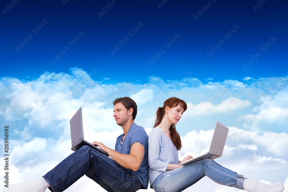 Couple both using laptops separately  against bright blue sky over clouds