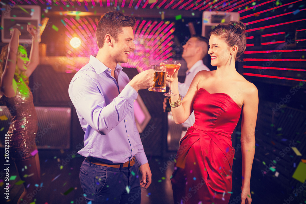 Smiling couple toasting glass of beer and cocktail against flying colours