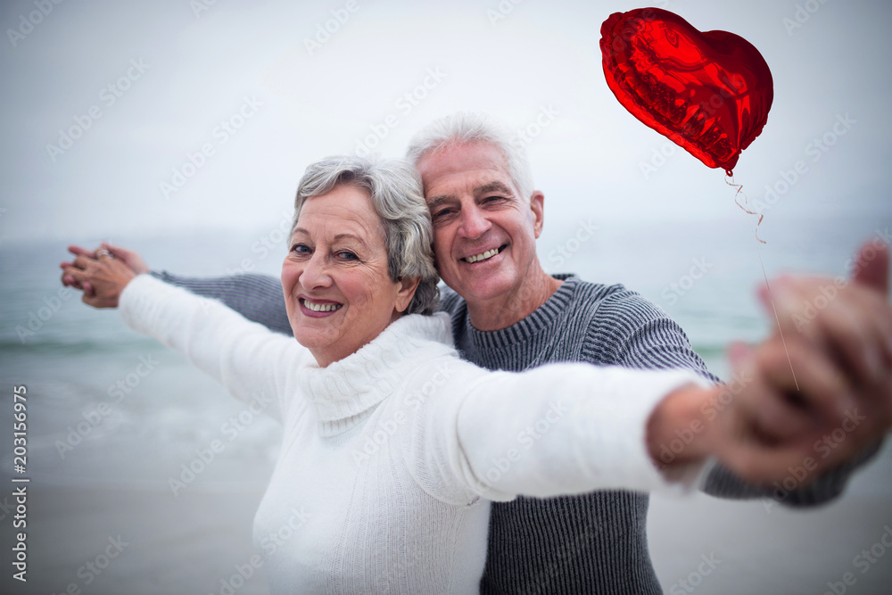 Red heart balloon against portrait of happy senior couple with arms outstretched 3d