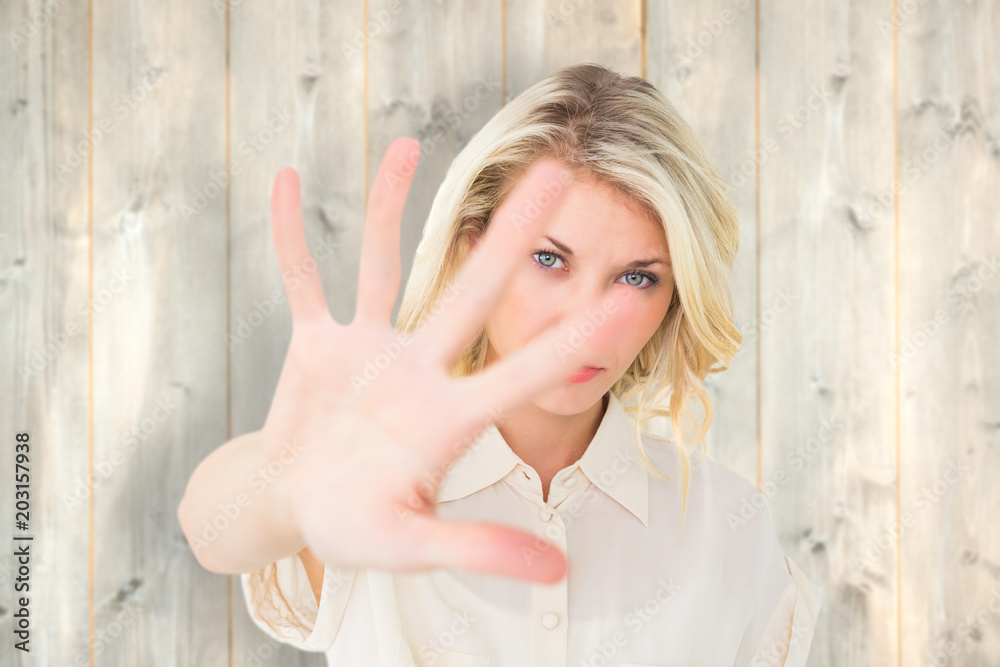 Pretty blonde holding hand up to camera against pale wooden planks