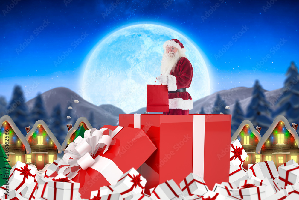 Santa standing in large gift against quaint town with bright moon