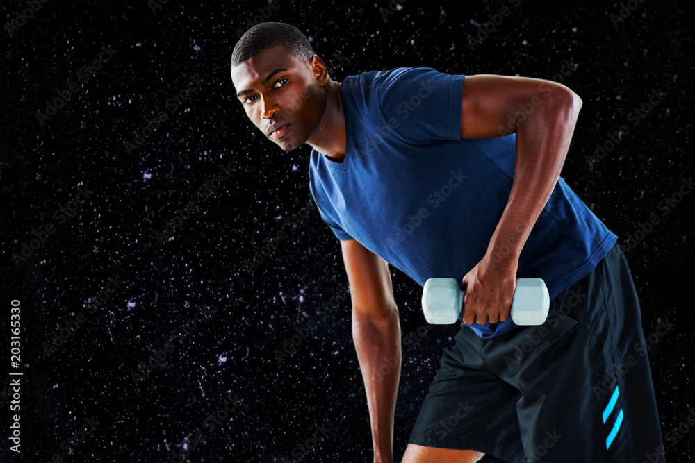 Portrait of casual young man lifting dumbbell against black background