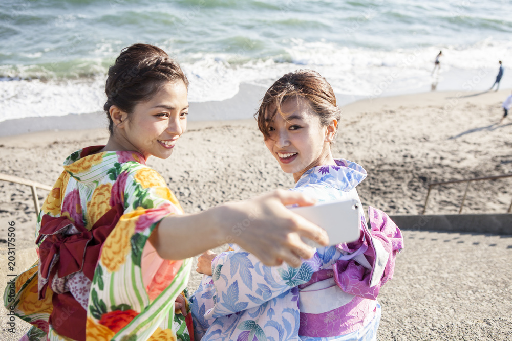 和服女性たちは海辺で写真を撮っている