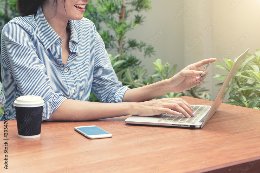 Asian shopper girl buying online with a laptop and credit card sitting in garden at home.