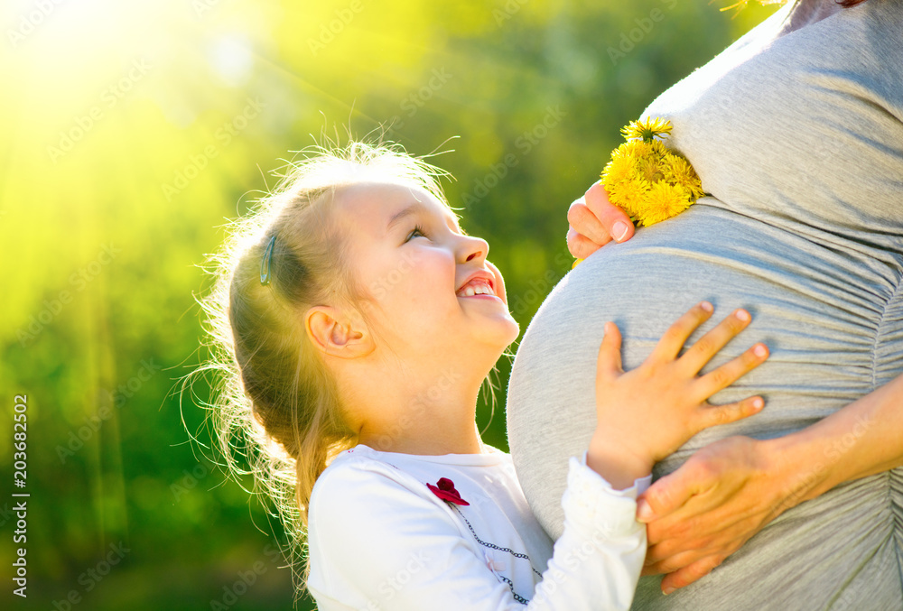 在阳光明媚的大自然中，孩子在妈妈肚子里听宝宝说话。快乐的孕妈妈wi