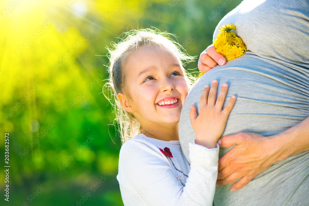 在阳光明媚的大自然中，孩子在妈妈肚子里听宝宝说话。快乐的孕妈妈wi