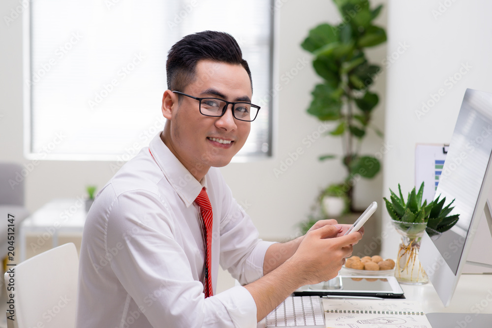 Man using computer and smart phone at the table in office against the window