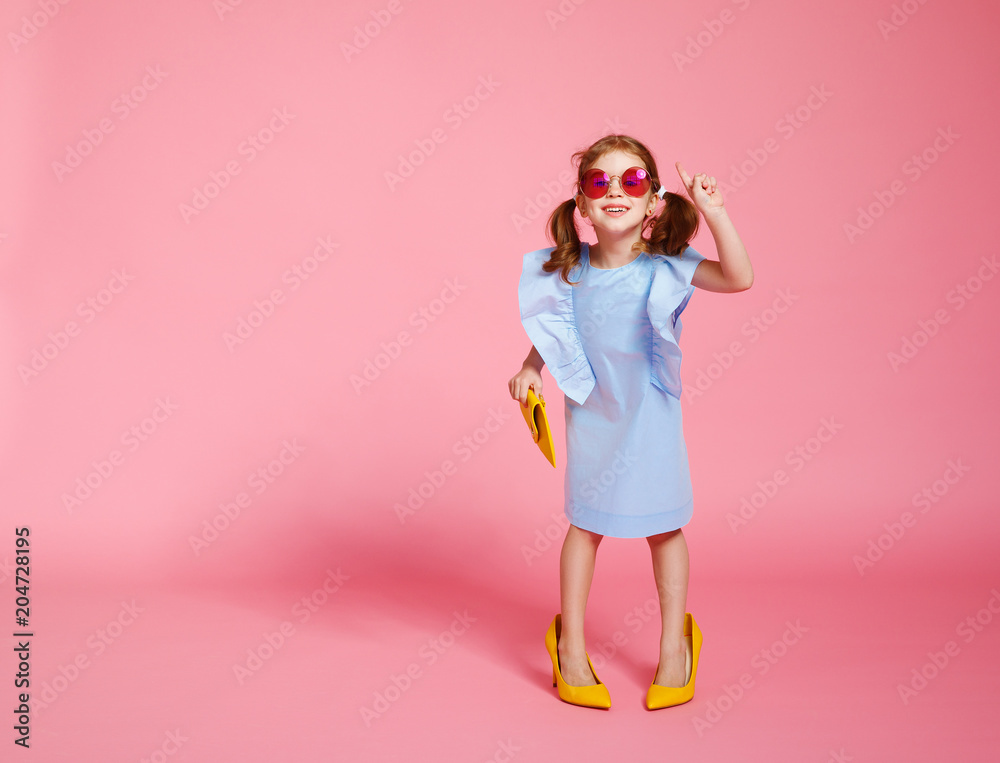 funny child girl fashionista in big mothers   shoes on colored background