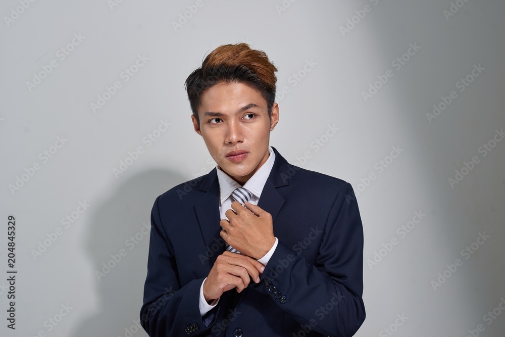 Confident businessman straightening his tie over gray background and looking at camera