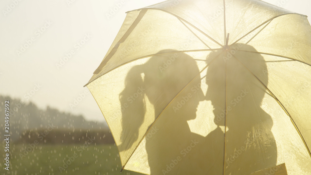 特写：恋爱中的男女躲在雨伞后面，准备接吻。